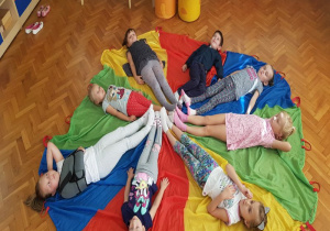 dzieci leżą na chuście animacyjnej w kolorach pór roku, każdy na swoim kolorze, nogami w kierunku do środka chusty